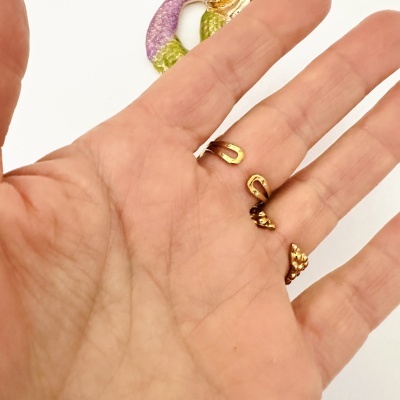 Mão com anel dourado aberto e objeto decorativo colorido ao fundo