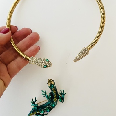 Colar dourado com cabeça de cobra cravejada e broche de lagarto verde com pedras