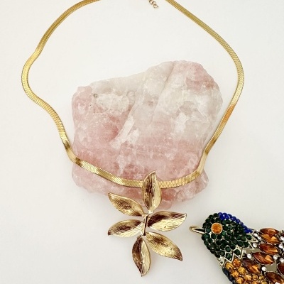 Colar dourado com pendente de flor sobre pedra rosa e broche de pássaro colorido