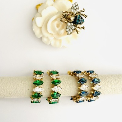 Broche flor branca com abelha dourada e pérolas, e quatro anéis com pedras coloridas em fundo branco