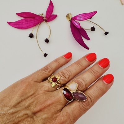 brincos com folhas rosas e hastes douradas acima de mão com unhas vermelhas