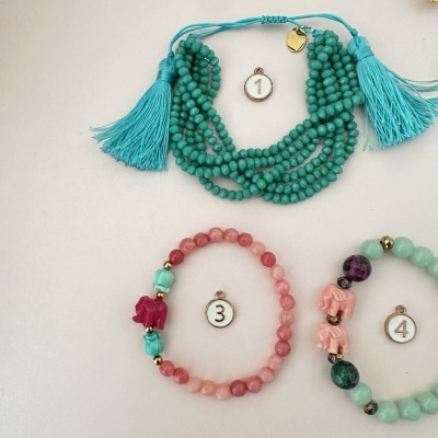 Três pulseiras coloridas com contas e tasséis, numeradas 1, 3 e 4 sobre fundo claro.