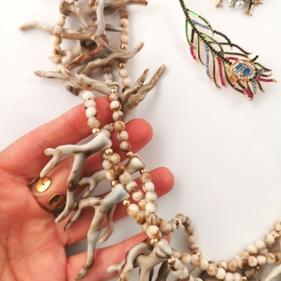 Colar com contas creme e pendentes de coral cinza na mão, bijuterias decorativas ao lado