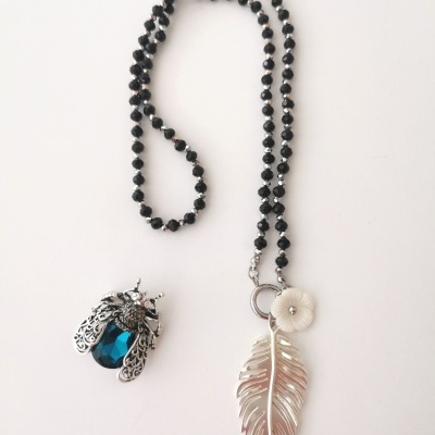 Colar com contas pretas, pendente folha prateada e flor branca, broche em forma de inseto com asas prata e corpo azul.