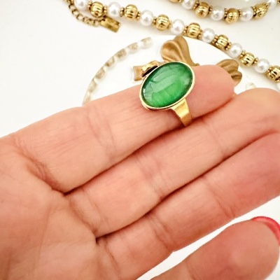 Anel dourado com pedra verde e colar de pérolas em fundo branco