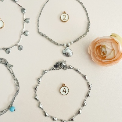 Pulseiras prateadas com pendentes e etiquetas numeradas, em fundo claro com flores