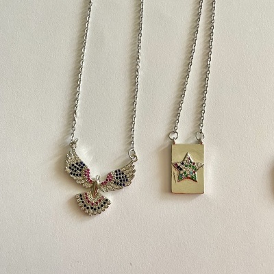 Colares com pendentes coloridos em prata e dourado sobre fundo claro.