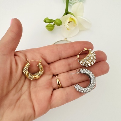 Brincos de argola dourados e prateados com pedras brilhantes numa mão