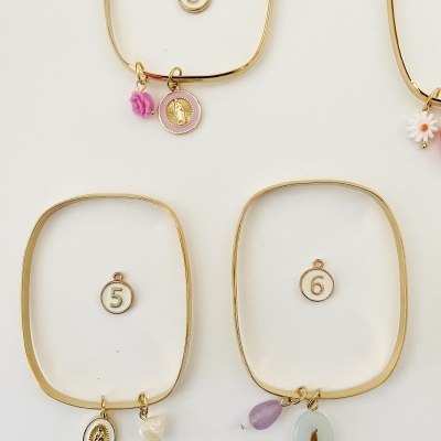 Pulseiras douradas com pendentes coloridos e pendentes numerados em fundo branco