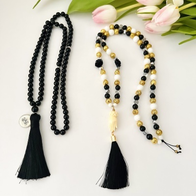 Dois colares de contas com franjas pretas e flores rosa no canto superior direito.