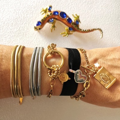Braço com múltiplas pulseiras de metal dourado e prateado e lagarto decorativo na parede