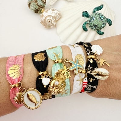 Pulseiras de tecido com pendentes dourados e conchas naturais ao fundo