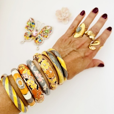 Mão com várias pulseiras coloridas e anéis dourados sobre fundo branco