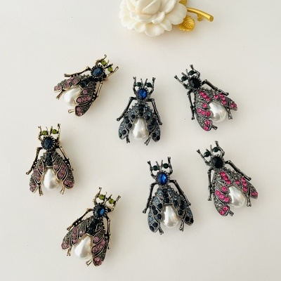 Broches em forma de moscas com pedras coloridas e pérolas junto a prender de cabelo dourado com flor branca