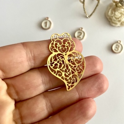 Bijuteria dourada em forma de coração com padrões recortados na mão e fundo com círculos numerados e anel