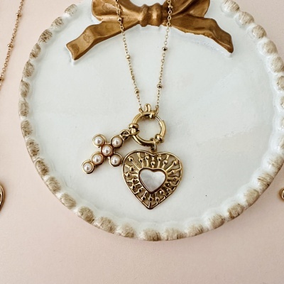 Colar dourado com pingentes de cruz e coração num prato branco decorativo