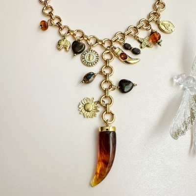 Colar com diferentes pendentes dourados e âmbar sobre fundo bege