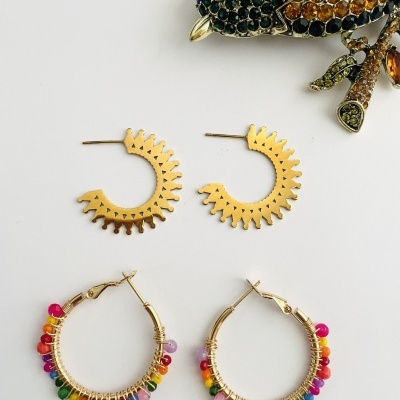 Dois pares de brincos dourados e broche de pássaro colorido sobre fundo branco