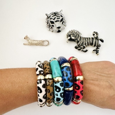 Pulseiras coloridas com padrão animal e três broches metálicos de animais em fundo branco.