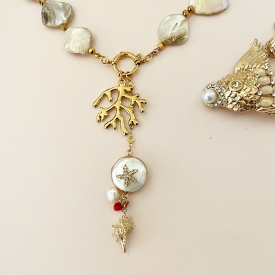 Colar dourado com contas e pendente marítimo sobre fundo claro