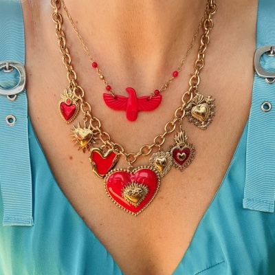 Colares dourados com pendentes em forma de corações e ave vermelha sobre blusa azul