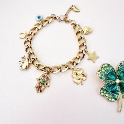 Pulseira dourada com vários pendentes temáticos e um trevo decorativo verde ao lado