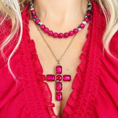 Colar com contas rosa e pendente cruz com pedras rosa sobre blusa rosa