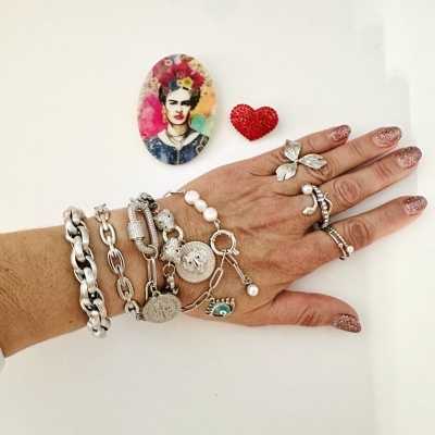 Mão com pulseiras e anéis prateados, unhas rosa glitter, imã de Frida Kahlo e coração vermelho em fundo branco