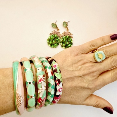 Mão com anel azul e pulseiras esmaltadas coloridas, brincos verdes em formato de abacaxi