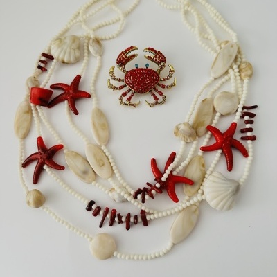 Colar com contas brancas, conchas e estrelas do mar, e broche de caranguejo vermelho.
