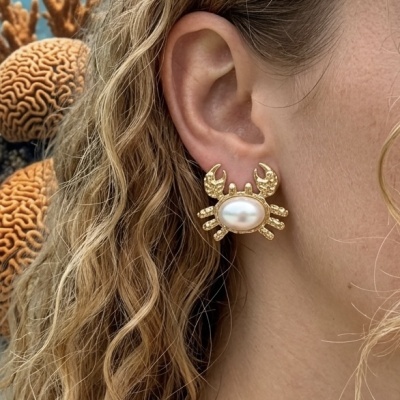 Brinco dourado em forma de caranguejo com pérola no centro, usado na orelha.