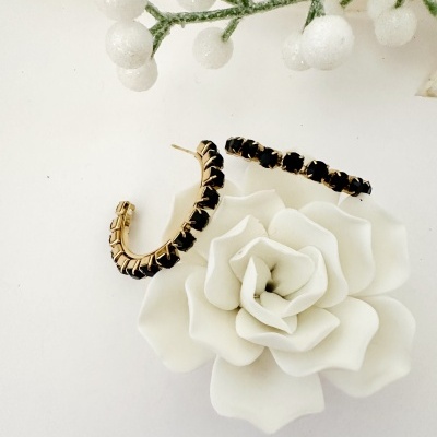 Brincos argola dourados com pedras pretas sobre flor branca