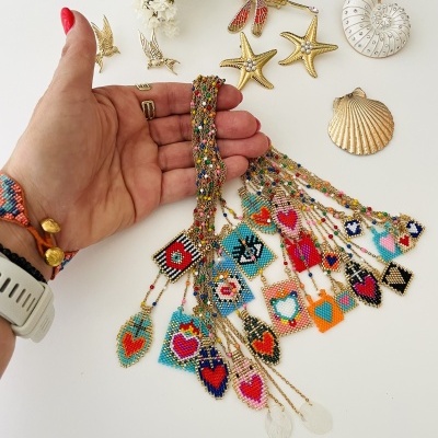 Conjuntos de colares coloridos de contas com padrões variados exibidos na mão, com acessórios dourados e flores secas ao fundo.