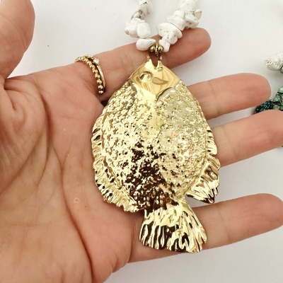 Colar com pendente dourado em forma de peixe e corrente de pedras brancas na mão