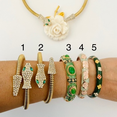 Colar dourado com pendente de flor branca e cinco pulseiras coloridas numa mão.