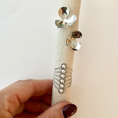 Dois anéis em metal prateado num suporte de tecido claro com mão segurando.