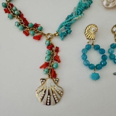 Colar e brincos com contas azuis e vermelhas, pendente em forma de concha, base branca e dourada.