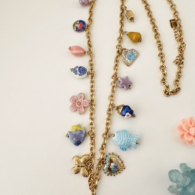 Colar dourado com pendentes coloridos de cerâmica em forma de peixes e flores sobre fundo branco
