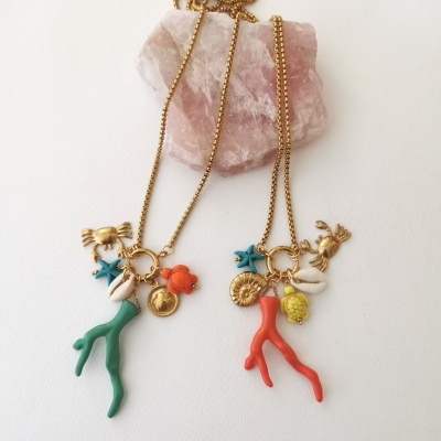 Dois colares dourados com pendentes de corais, estrelas do mar, conchas e pequenos animais em fundo branco com pedra rosa