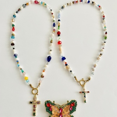 Dois colares coloridos com pendentes de cruz e borboleta sobre fundo branco.