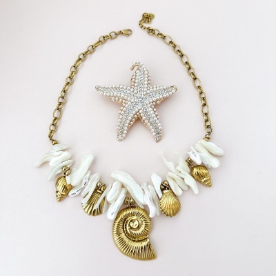 Colar com conchas douradas e pérolas brancas, com estrela do mar decorativa atrás