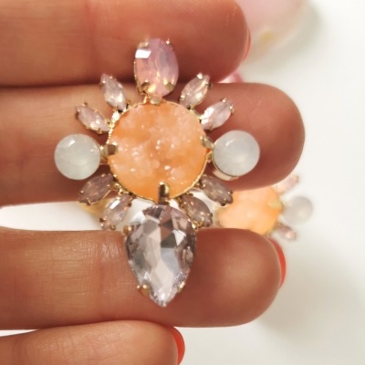 Brincos com pedras coloridas e base dourada entre dedos