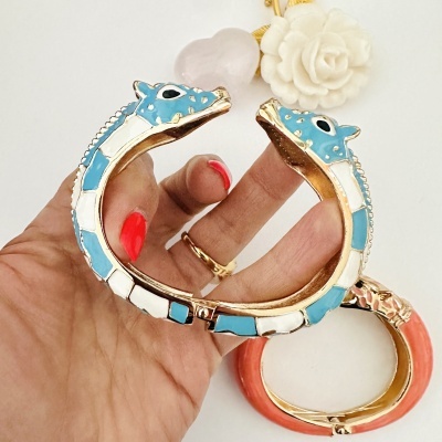 Pulseira com cabeça de dragão em esmalte azul e branco e metal dourado sobre fundo branco com flores.
