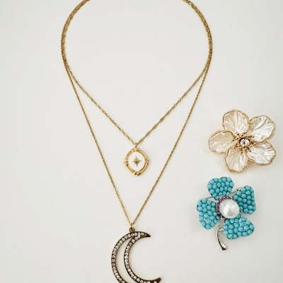 Colar dourado com dois pendentes e dois broches em forma de flores, um dourado e outro azul com pérola.