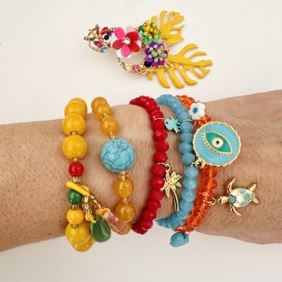 Pulseiras coloridas com contas e pingentes variadas no braço.