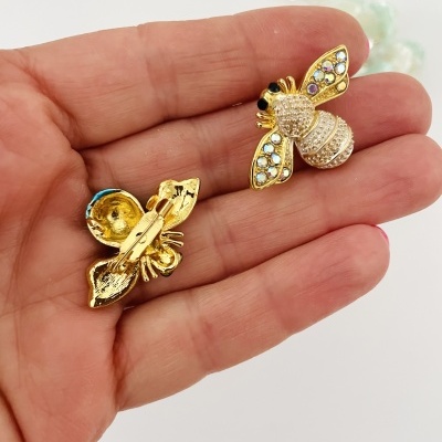 Brincos dourados em forma de abelha com pedras brilhantes azuis e brancas numa mão