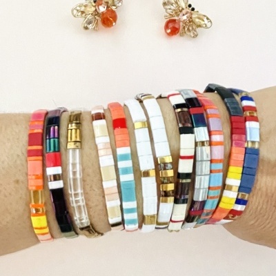 Pulseiras coloridas de contas quadradas usadas no pulso com brincos de abelha ao fundo