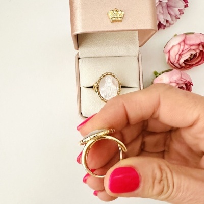 Anel dourado com imagem religiosa em caixa rosa com flores cor-de-rosa