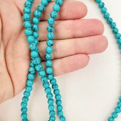 Colar ou pulseira com contas azuis turquesa, douradas e vermelhas numa mão