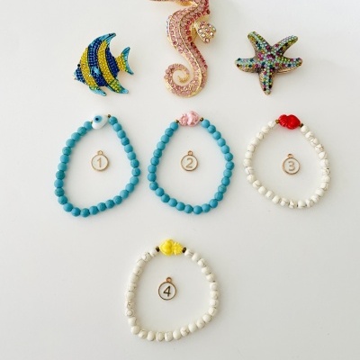 Três broches de peixe coloridos e quatro pulseiras numeradas em contas azuis e brancas num fundo branco